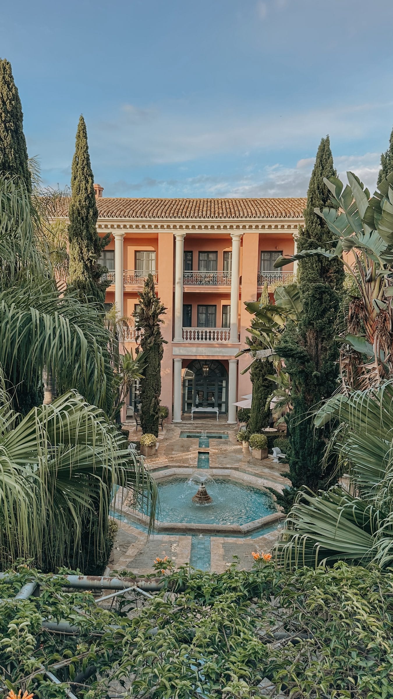 The terracotta facade of Anantara Villa Padierna seen from its formal gardens, framed by palms and cypresses