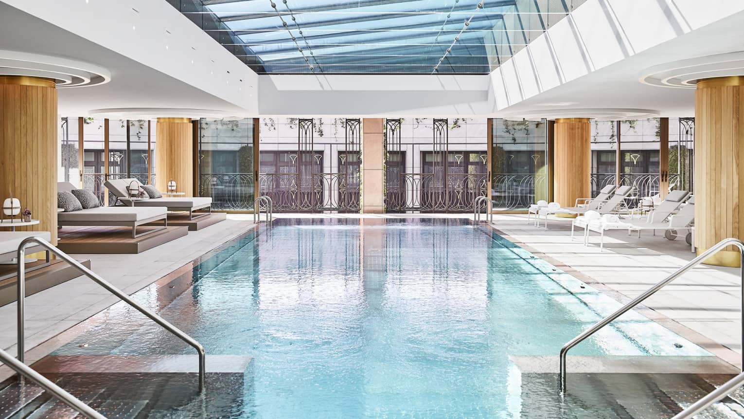 The indoor swimming pool at Four Seasons Madrid, under a glass skylight with wooden columns and loungers alongside