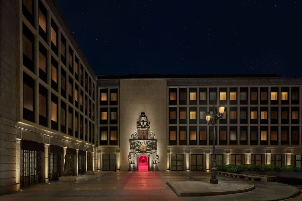 The floodlit limestone facade of The Madrid EDITION at night, with a red-lit baroque doorway